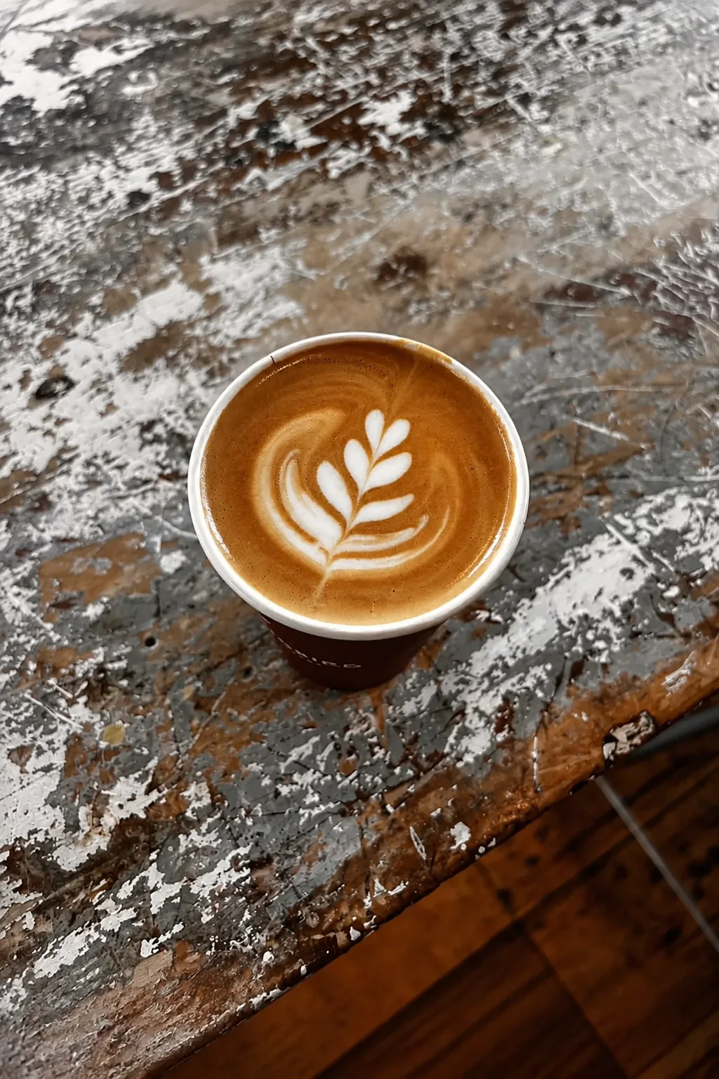 Latte art in a cup on a worn wooden table
